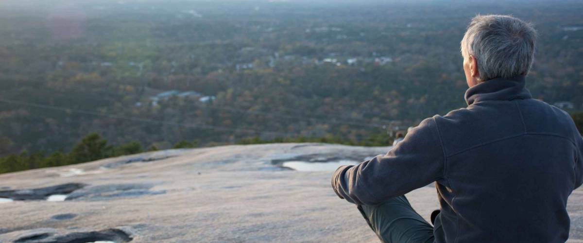 An elderly man practices concentration and prays on top of a mountain at sunset