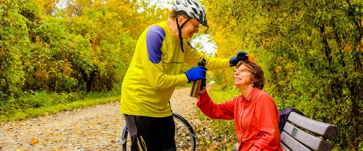 Laughing senior bicyclist brushing fallen leaf off his wife's hair