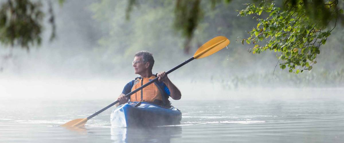 Mature adult man kayaking alone in Vermont on a foggy morning