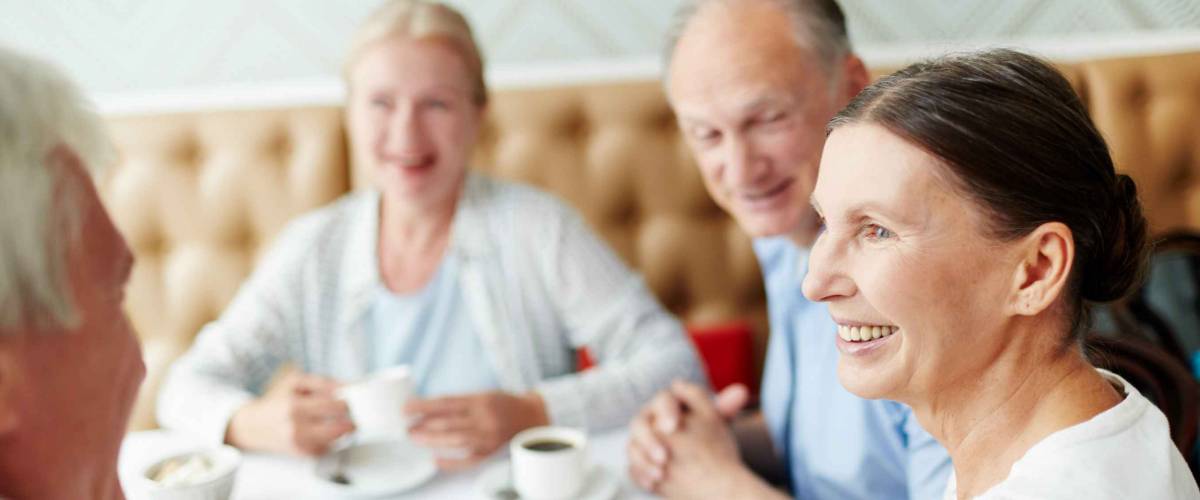 Group of senior companions sitting by table in cafe and having talk by cup of coffee