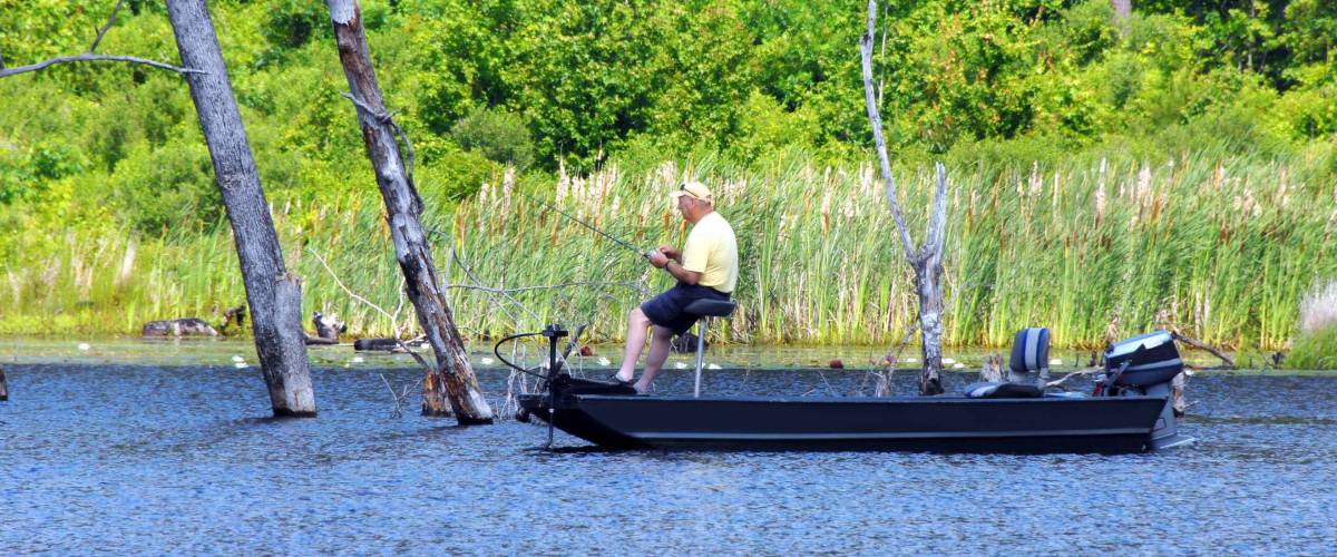 Fisherman trolls a new lake in privately owned in south arkansas called Cooty Lake. He is fishing for bass alone in his boat. He is wearing a yellow shirt and cap.
