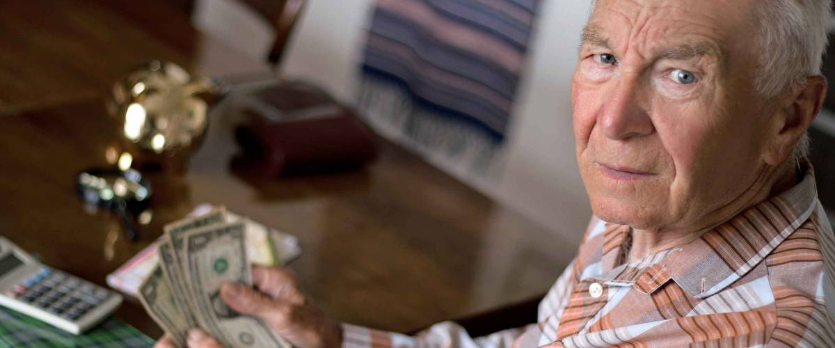 Unhappy elderly man counting dollars in retirement