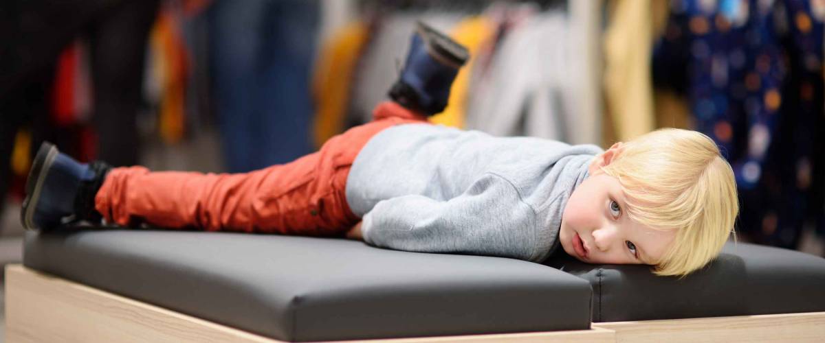 Tired little boy during shopping with parents. Fashion clothes for kids. Child in shopping center/mall or baby apparel store