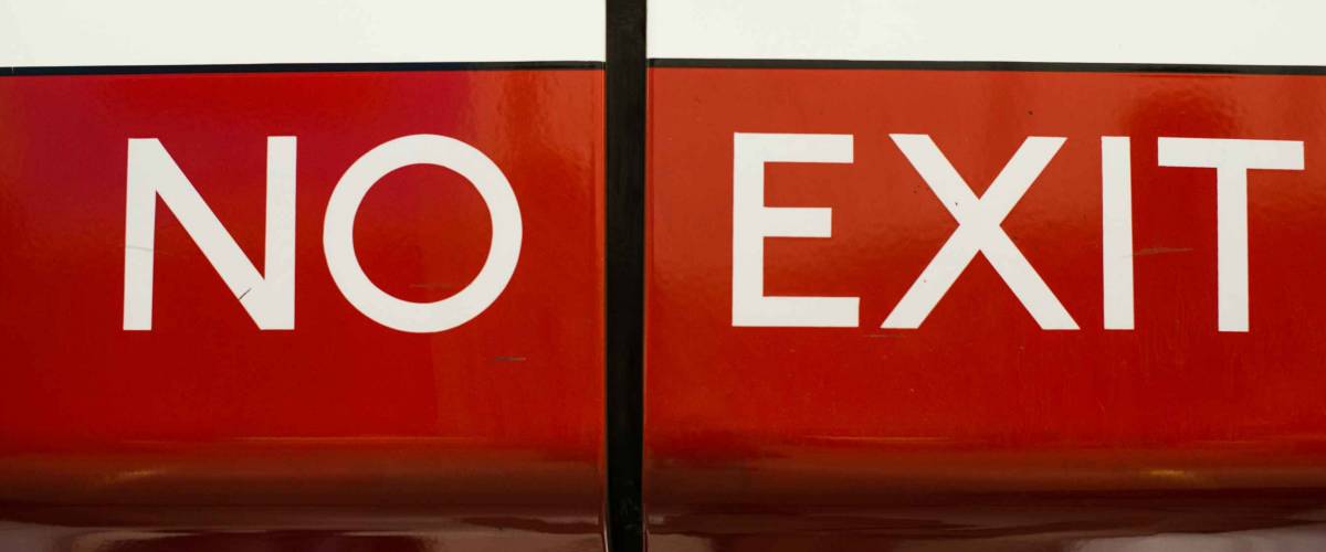 No Exit sign on a red metal barrier preventing somebody from leaving by that route