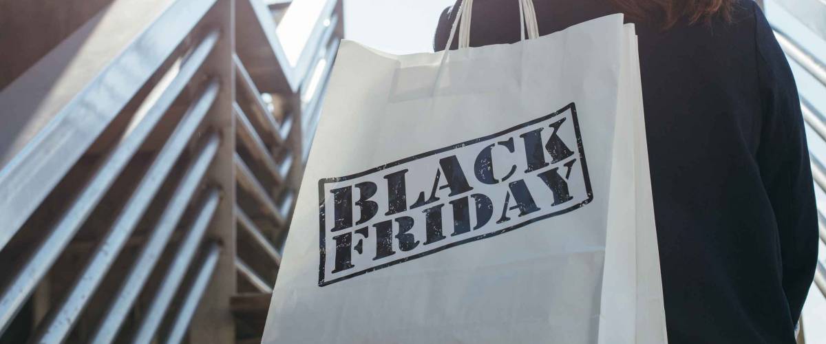 Rear view of incognito brunette holding Black Friday shopping bag while standing outdoors. Copy space