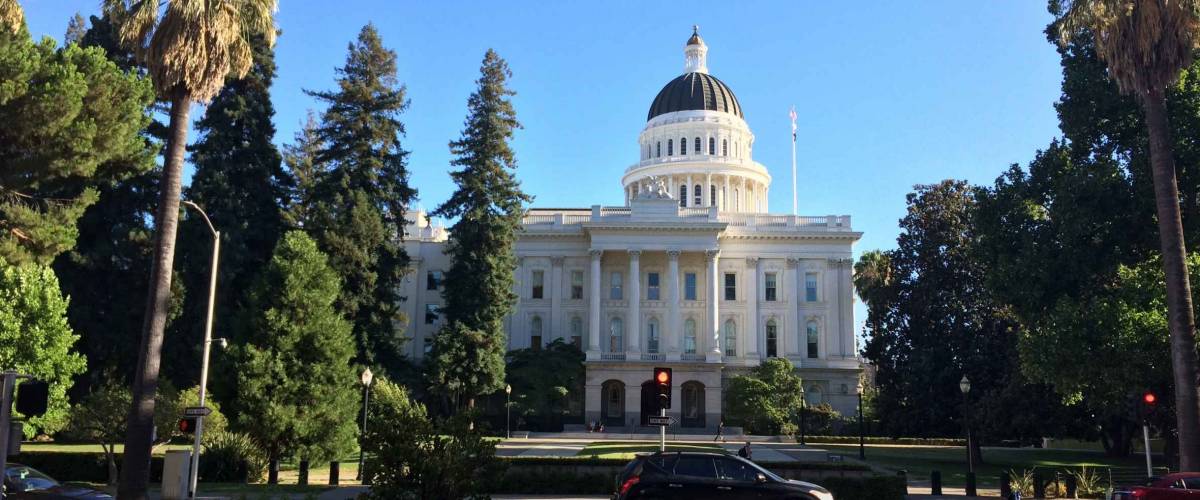 Palm trees swaying and cars driving by the California State Capitol building in Sacramento, CA
