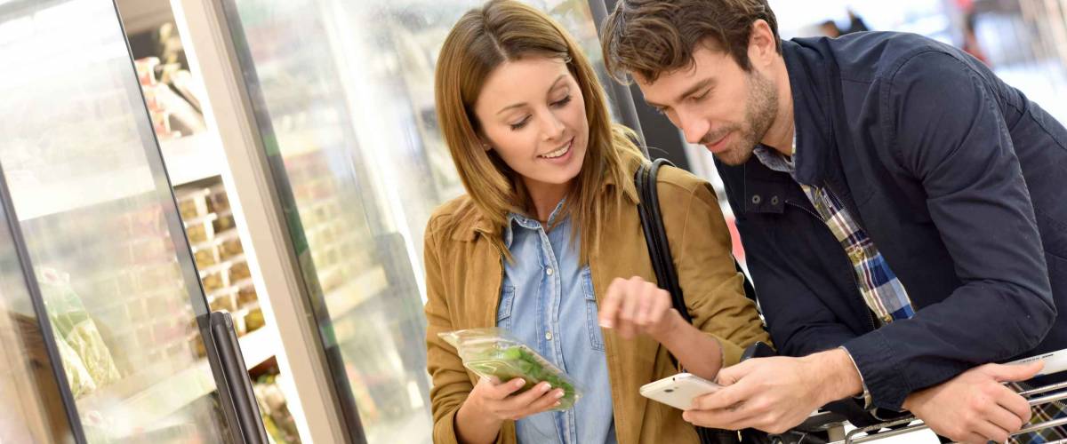 Couple in supermarket reading shopping list on smartphone