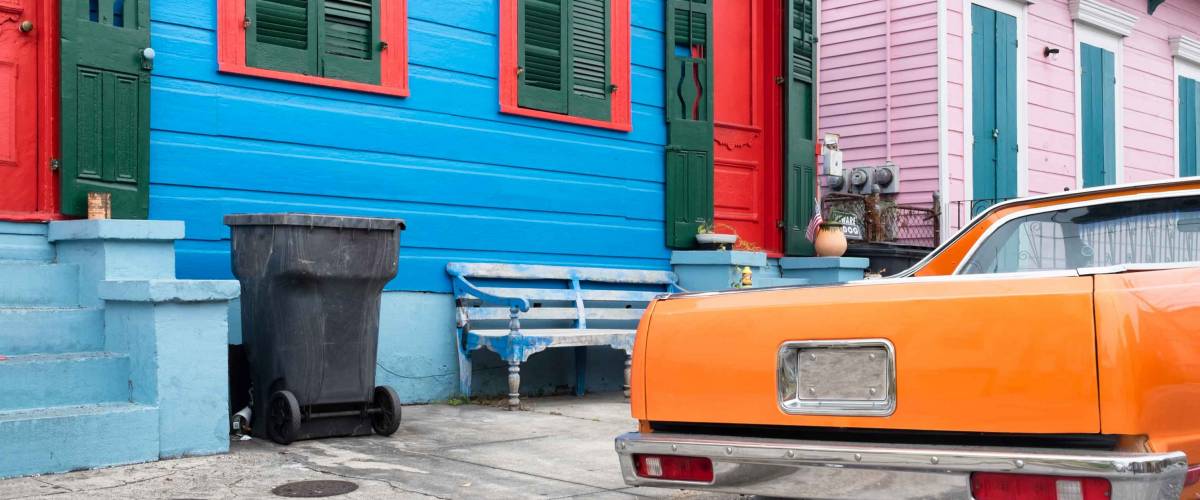 New Orleans colorful vintage painted houses and a classic orange car parked in front. Typical shotgun architectural style of homes seen in the historic neighborhoods.