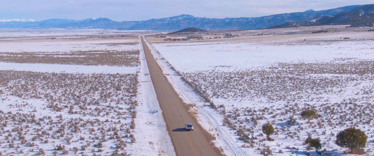 DRONE Flying behind a silver car driving along the straight highway running across the snowy countryside of Montana.