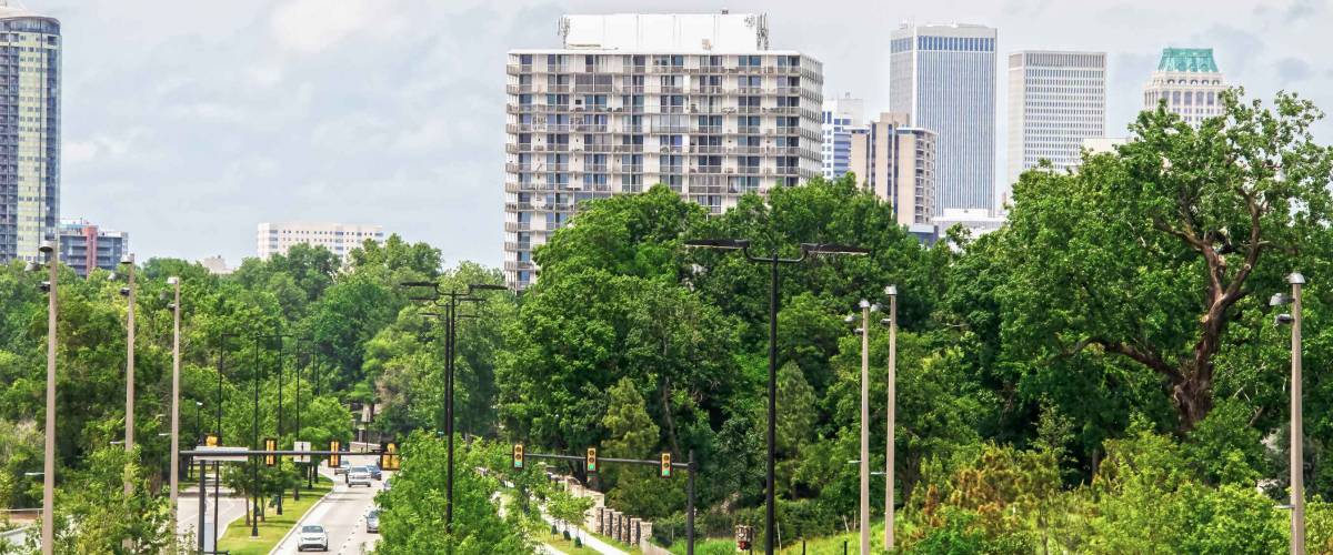 Divided highway with lots of lush foliage and green stoplight with cars and trucks and pedestrians leading to downtown Tulsa Oklahoma USA