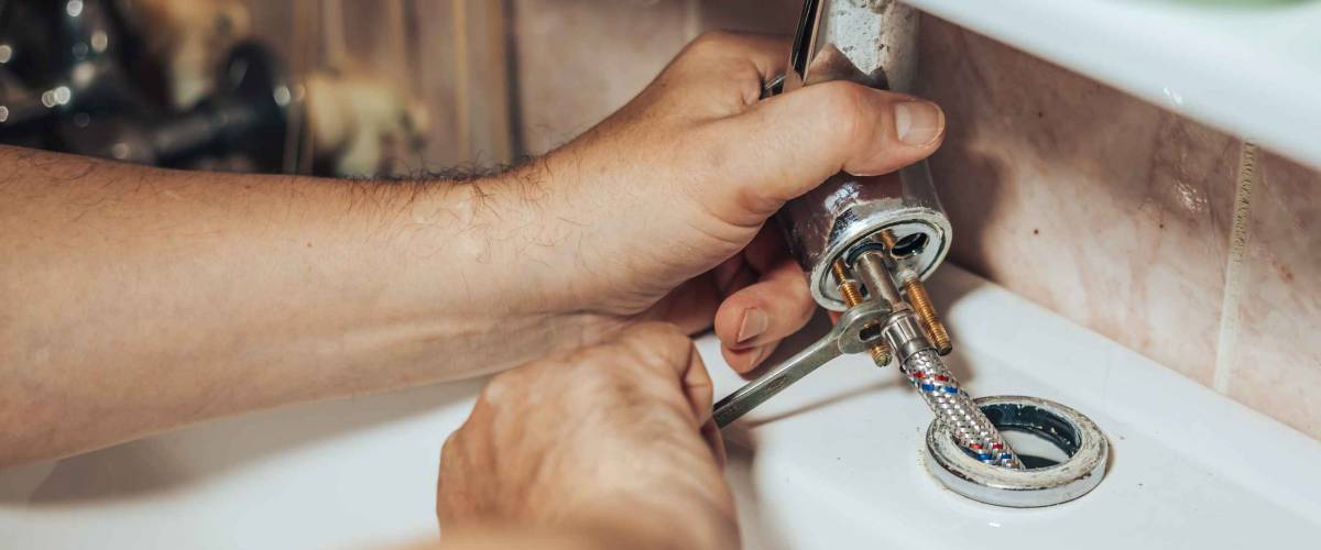 Man services and repairs leaky old faucet on the tap in the bathroom