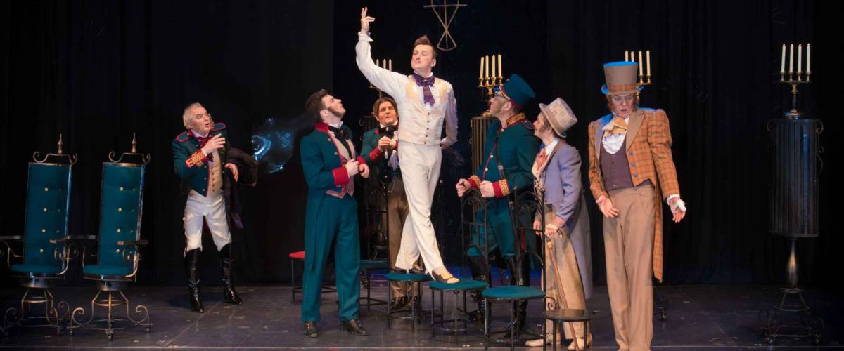 Actors, men in old clothes frock coats and uniforms and women in medieval dresses with lush skirts posing on stage in the background of scenery