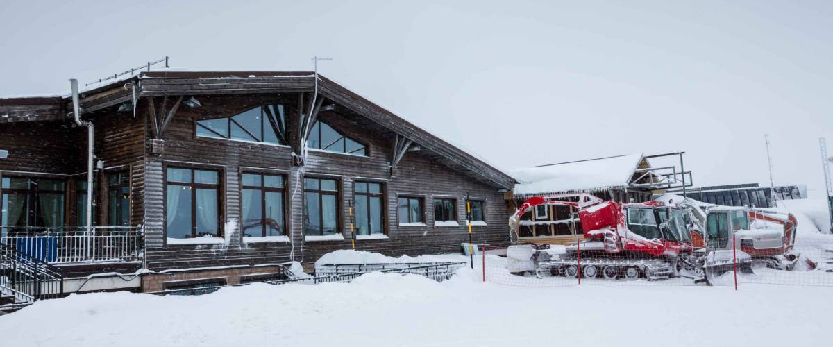Guest house in a snowy ski resort and a nearby snowcat and other specialized tracked vehicles in windstorm