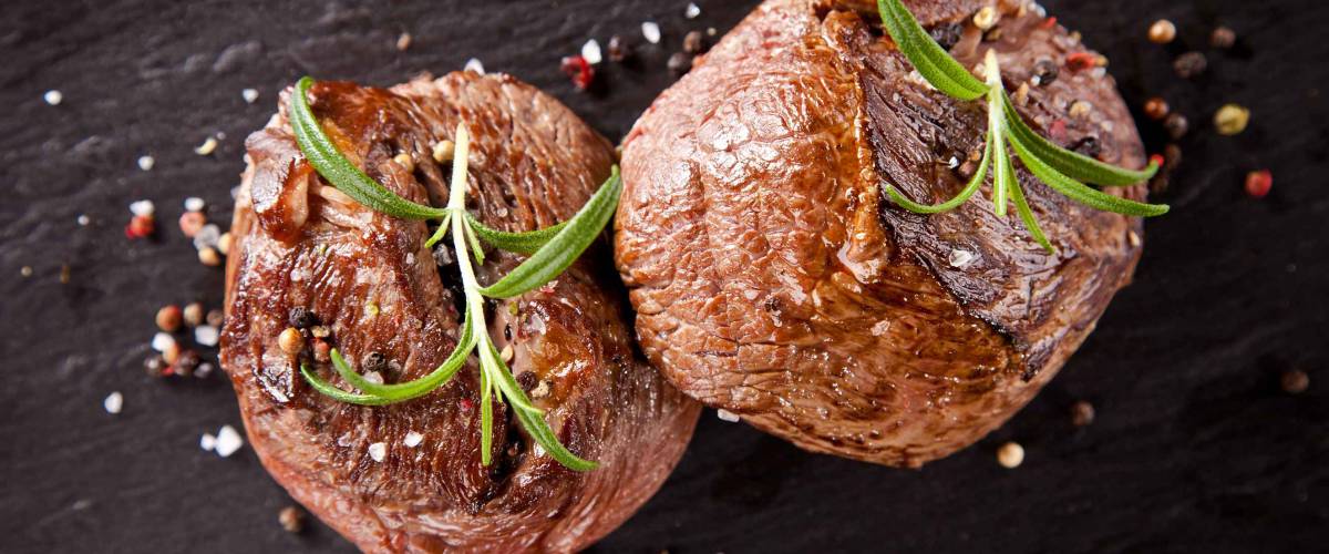 Pieces of red meat steaks with rosemary served on black stone surface. Shot from upper view