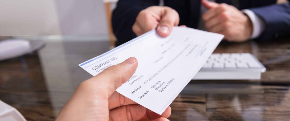 Close-up Of A Businessperson's Hand Giving Cheque To Colleague At Workplace