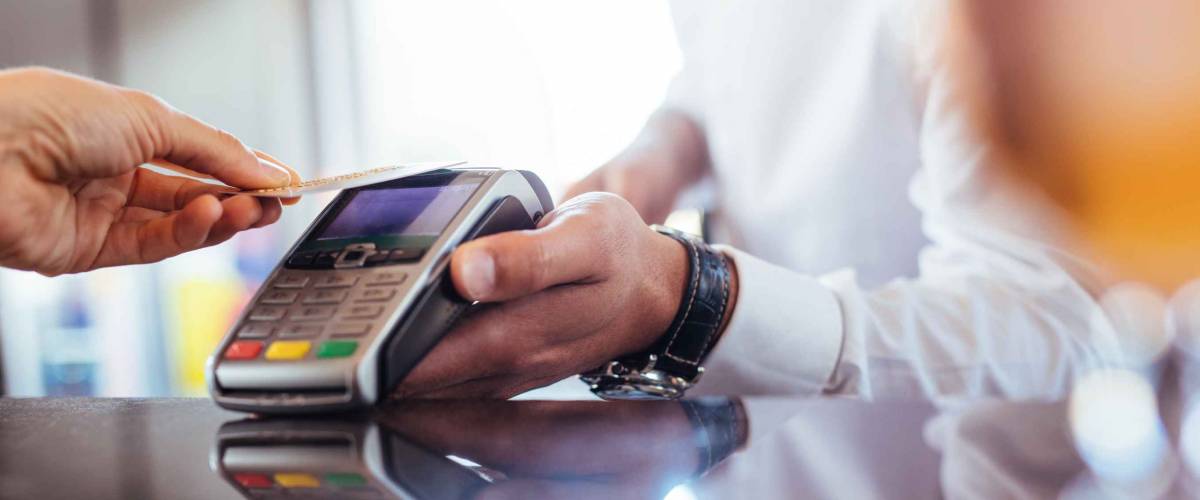 Hand of customer paying with contactless credit card with NFC technology. Bartender with a credit card reader machine at bar counter with female holding credit card. Focus on hands.