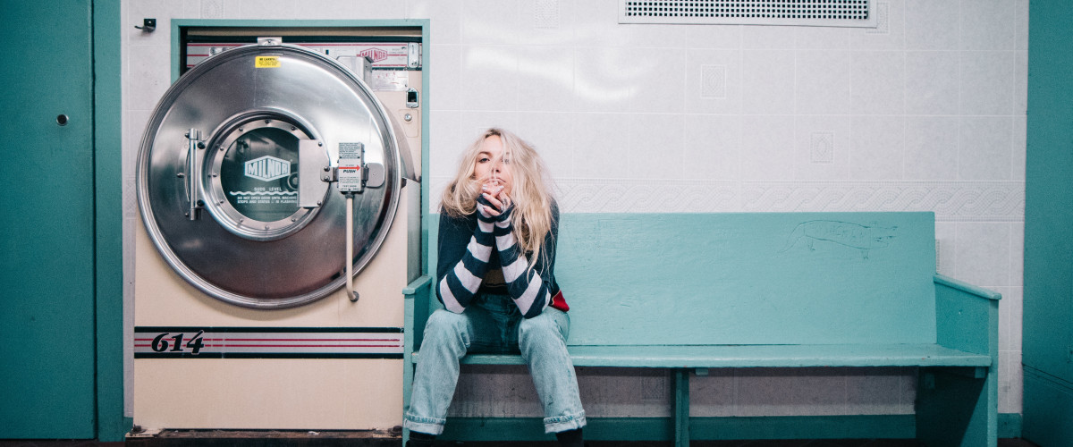 Young woman waiting for her laundry to finish in an old laundromat