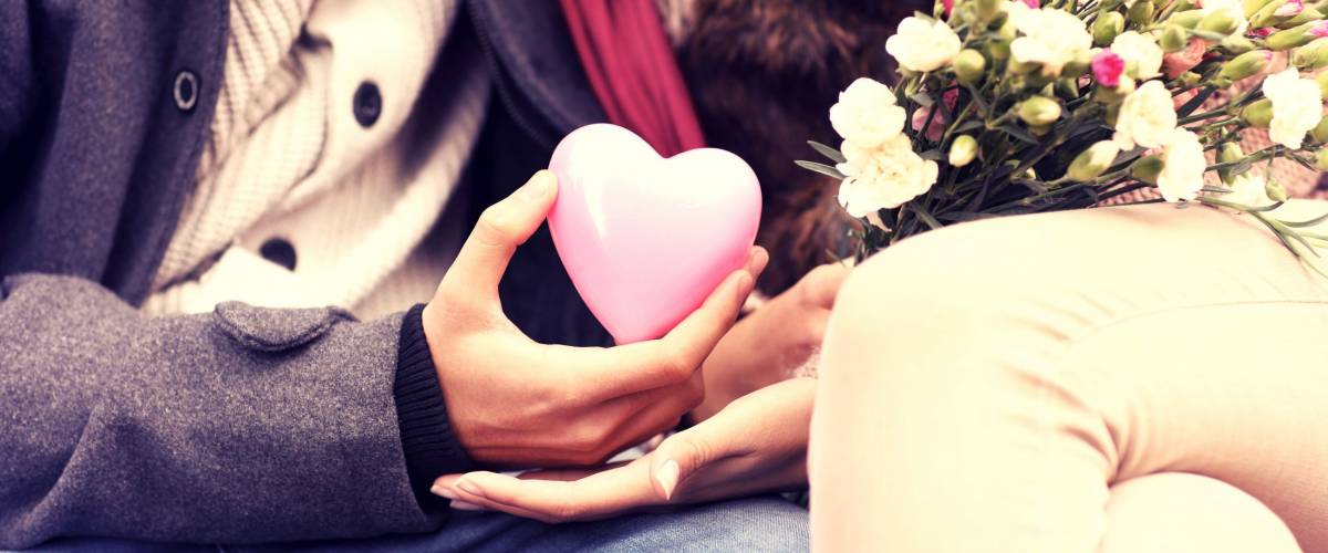 A midsection of a romantic couple sitting on a bench in the park holding Valentines gift and flowers