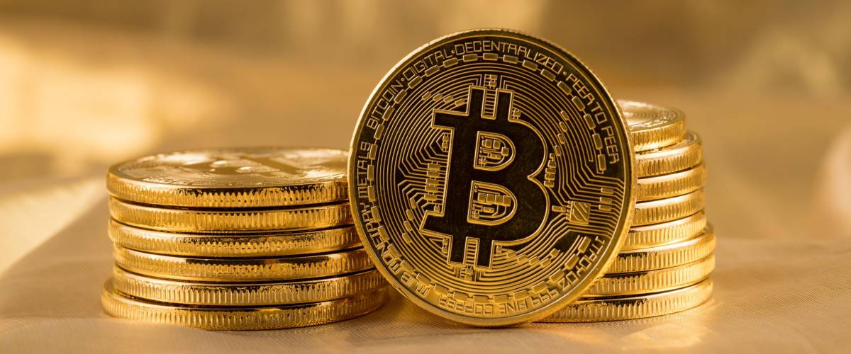 Stack of bitcoins with gold background with a single coin facing the camera in sharp focus with shading on the icon letter B on the face of the bit coin