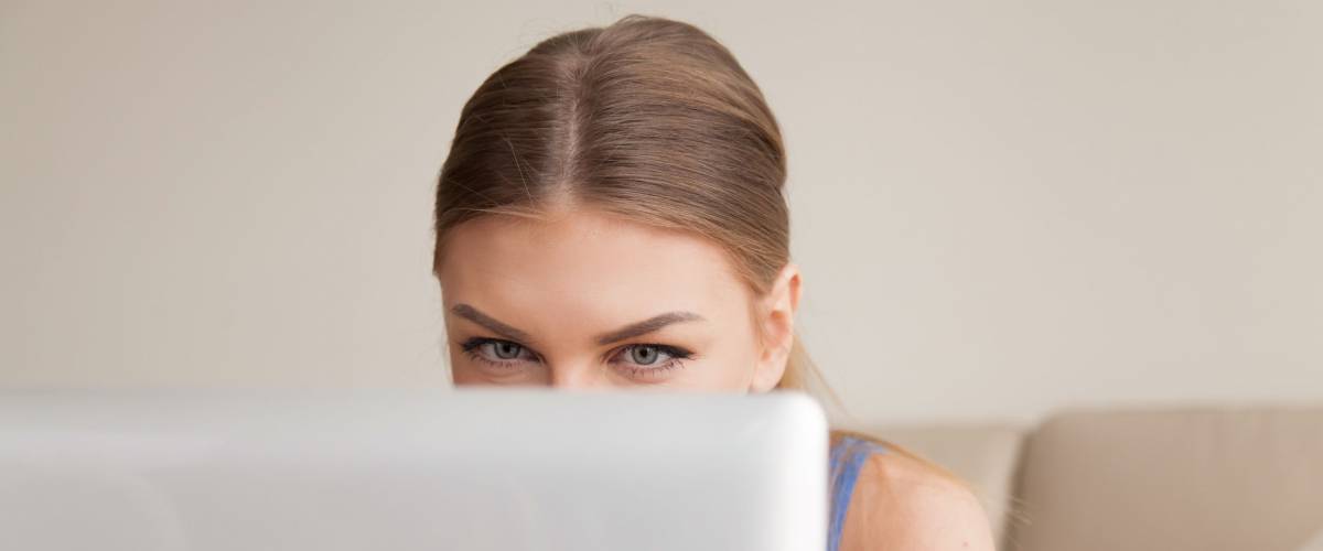 young funny girl peeking over top of laptop