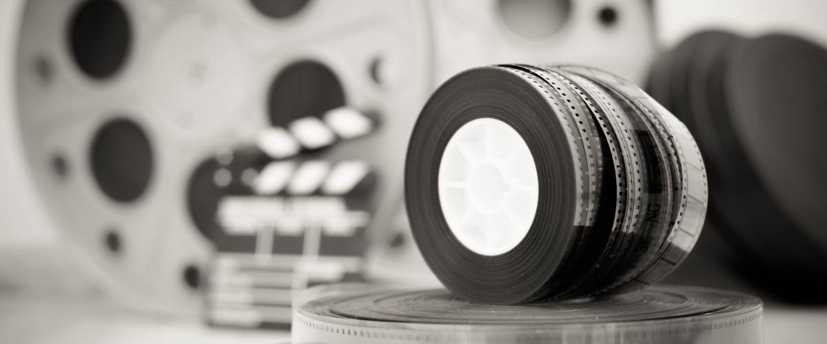 Heap of old 35 mm movie reels with out of focus clapper and boxes in background, vintage black and white