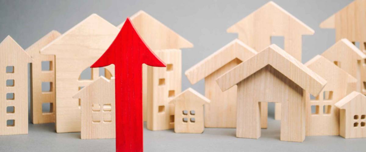 Red arrow up and miniature wooden houses. The concept of rising home prices.