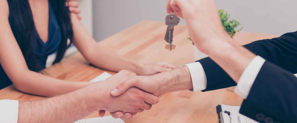 Close up photo of handshake. Broker giving keys of new house