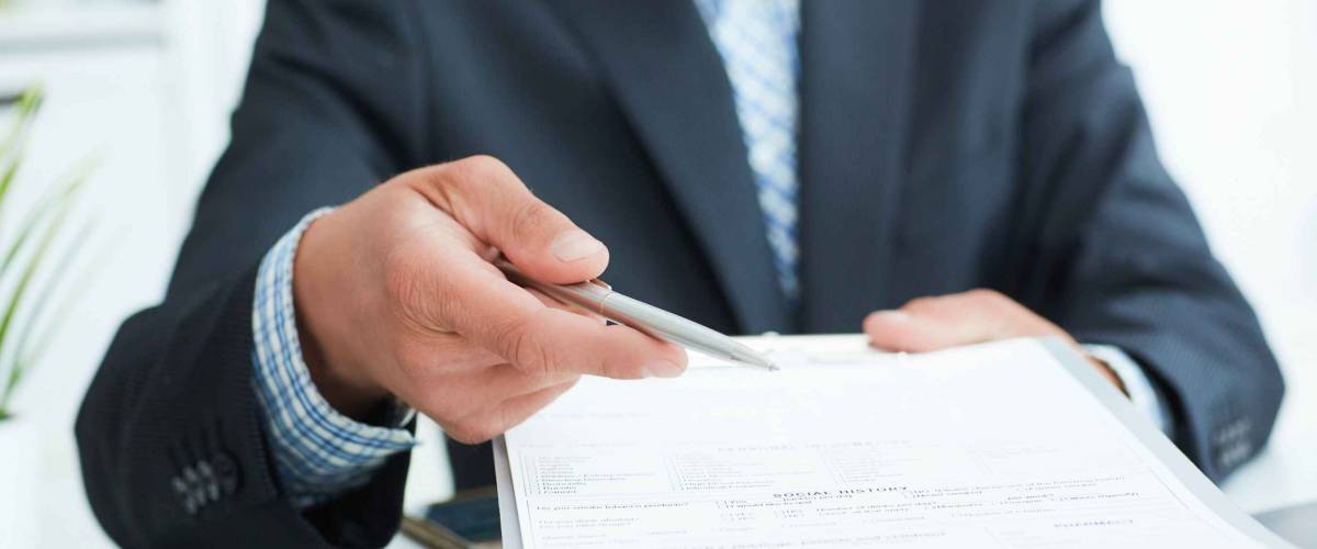 Man in a suit offers to sign a contract holding a pen and documents for signature