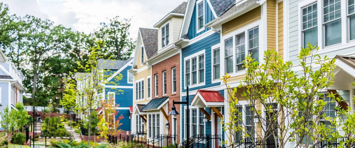 Row of colorful, red, yellow, blue, white, green painted residential townhouses, homes, houses with brick patio gardens in summer