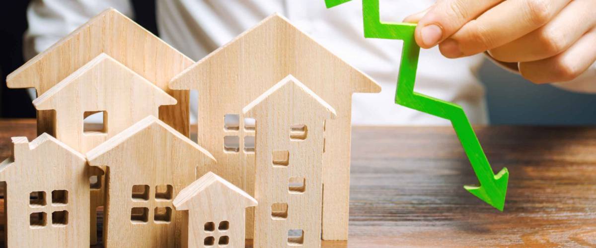 Analyst holds down arrow near the wooden houses. Concept of falling mortgage rates.