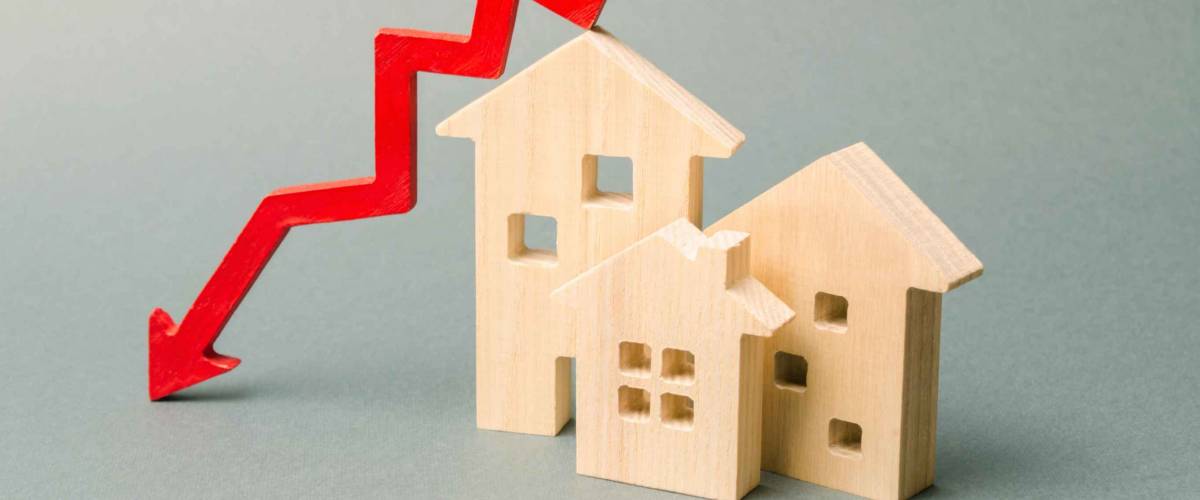 Miniature wooden houses and a red arrow down. The concept of lower mortgage rates.