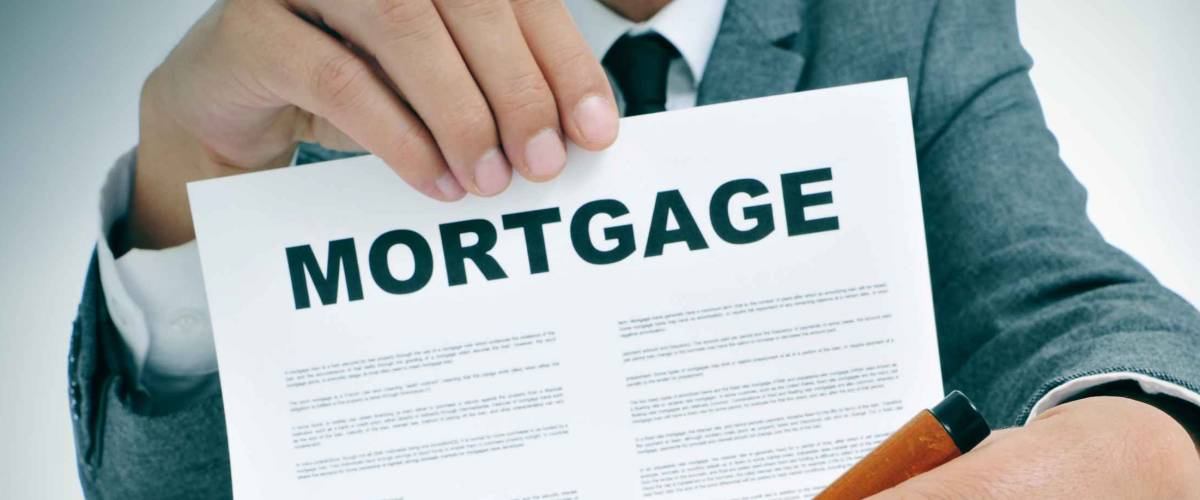 man wearing a suit sitting in a table showing a mortgage loan contract and where the signer must sign