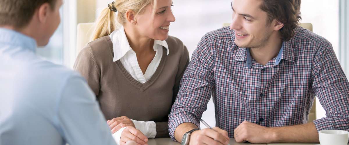 smiling young couple signing an agreement in the presence of a broker