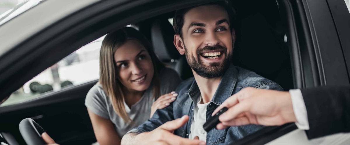 Happy beautiful couple is choosing a new car at dealership.