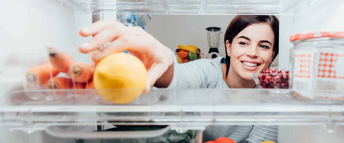 Smiling woman taking a fresh lemon out of the fridge, healthy food concept