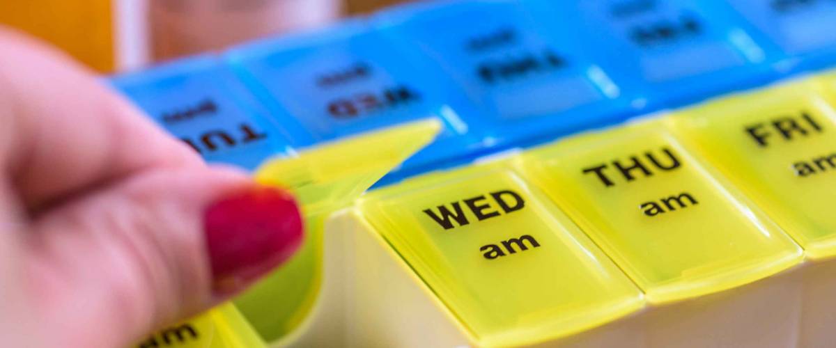 Close up of a woman's hand opening a pill holder for daily medications