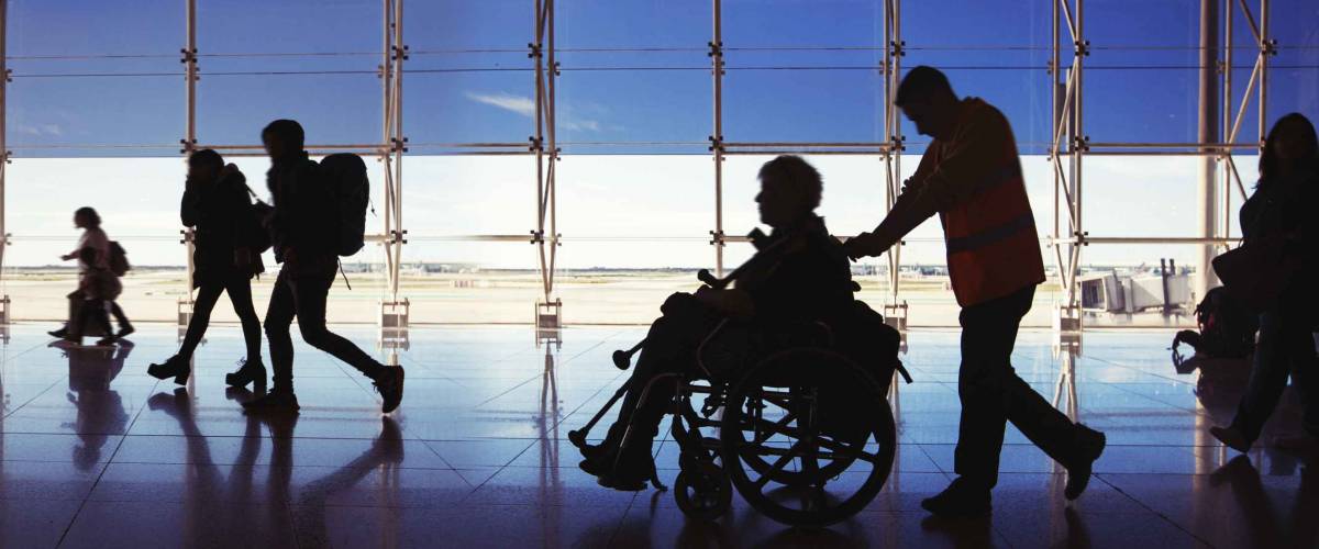 Silhouette of man in wheelchair and people carrying luggage and walking in an airport