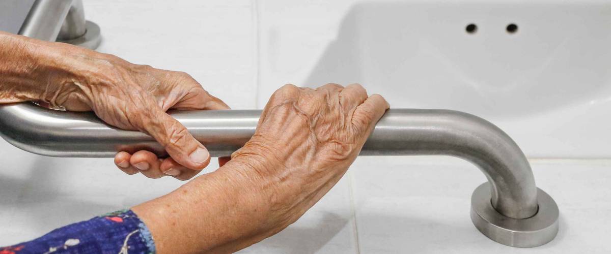 Elderly woman holding on handrail in bathroom