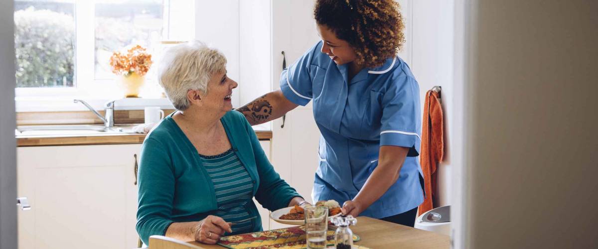 Care worker giving an old lady her dinner in her home.