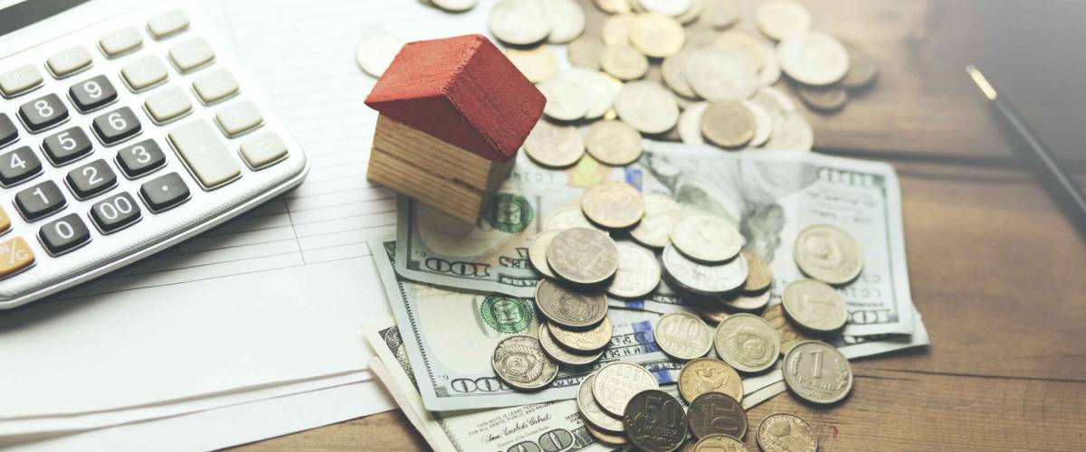Money, calculator and piggy bank with house model on table
