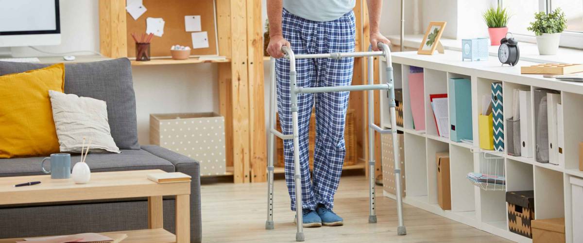 Portrait of senior man in domestic clothing trying to walk with walker in the room at home