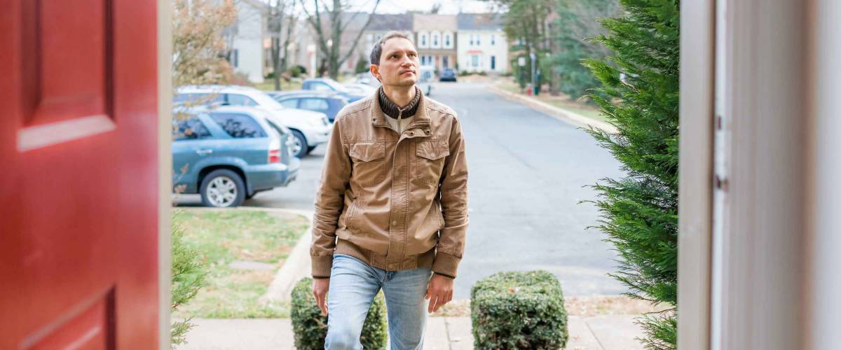 Young man standing on front porch frontyard steps in front of house home buyer looking to buy property