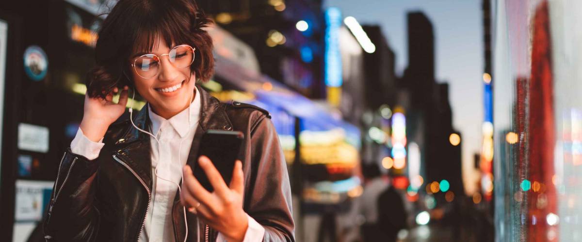Young woman in cool eyeglasses enjoying music on her new smartphone
