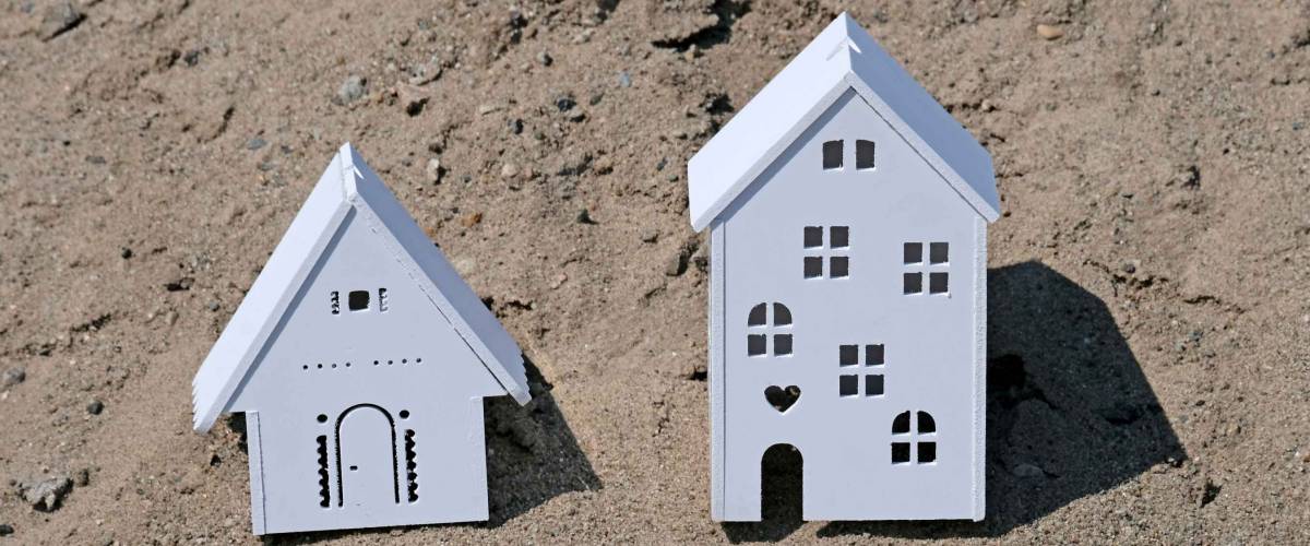Plastic white house large and small or residential model in nature. Souvenir house with Windows. The concept of construction or capital investment. Mortgage or loan concept. Sand background.