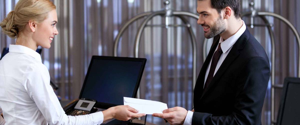 smiling receptionist giving envelope to businessman in hotel