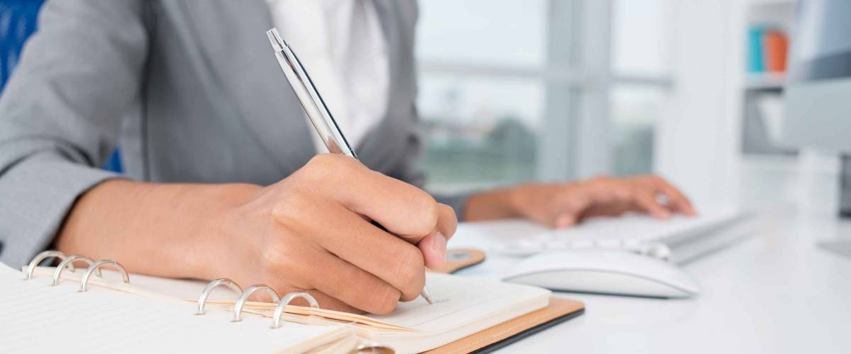 Close-up of female hands making notes in the notepad at office