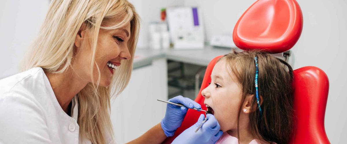 Cute little girl sitting on dental chair and having dental treatment.