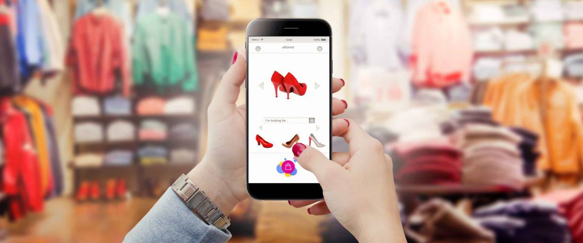 Woman in clothing store holding phone in hands and searching online shoes