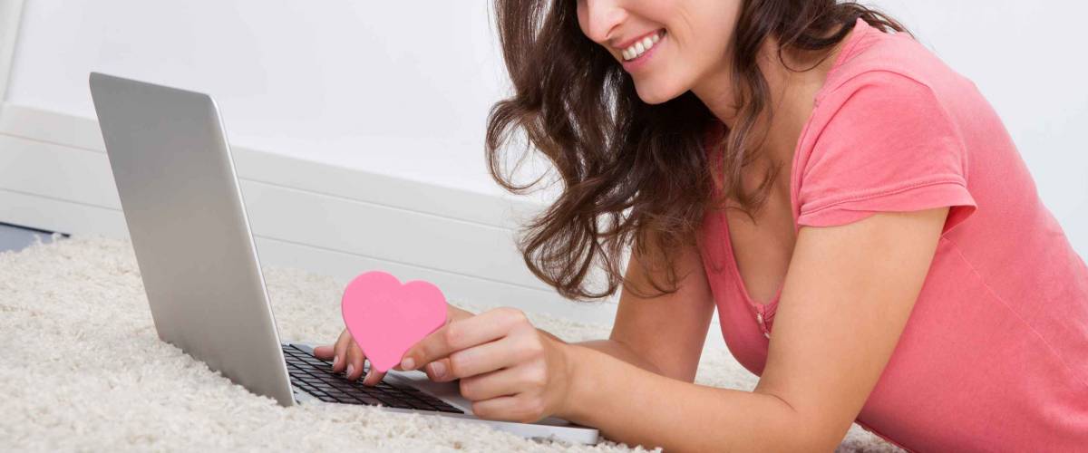 Portrait Of Smiling Young Woman Lying On Floor In Front Of Laptop