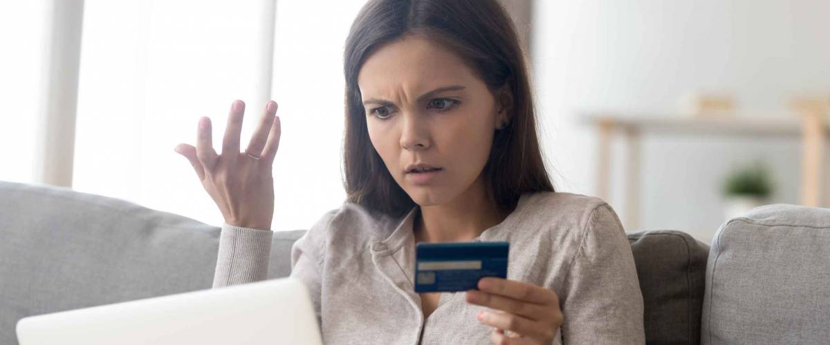 Upset young woman looking at computer while holding credit card